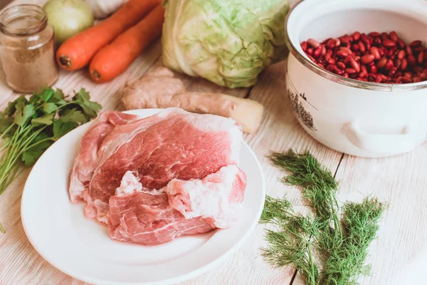 Food ingridients: red beans, carrot, cabbage, meat, onion, ginger for recipe stewed beans with meat on wooden background. Steps in cooking, process of preparing food. Concept of homemade healthy food.