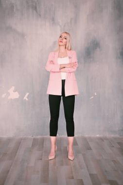 Doğrudan kameraya bakarak basık bir duvara poz güzel bir gülümseme ile pembe ceket ve pantolon çizgili pantolon giyen çekici olumlu orta yaşlı sarışın bir kadın. Moda düzeltisiz p