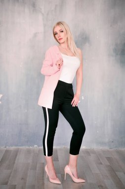 Doğrudan kameraya bakarak basık bir duvara poz güzel bir gülümseme ile pembe ceket ve pantolon çizgili pantolon giyen çekici olumlu orta yaşlı sarışın bir kadın. Moda düzeltisiz p