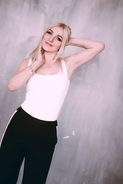 Attractive positive middle-aged blond woman wearing pink jacket and pants with trouser stripes with a beautiful smile posing against a receding wall looking directly at the camera. Fashion retouched p — Stock Photo, Image