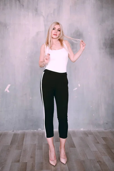 Attractive positive middle-aged blond woman wearing pink jacket and pants with trouser stripes with a beautiful smile posing against a receding wall looking directly at the camera. Fashion retouched p — Stock Photo, Image