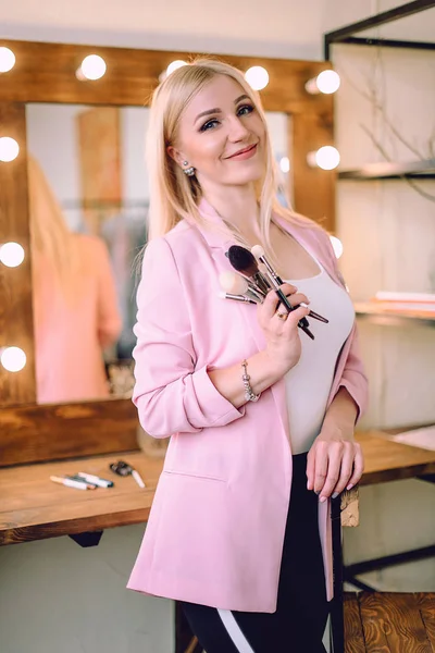 Make-up artist positive beautiful blonde woman posing near mirror in make-up room — Stock Photo, Image