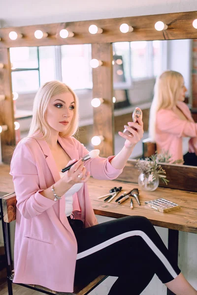 Portrait of a beautiful blonde woman applying makeup near a mirror — Stock Photo, Image