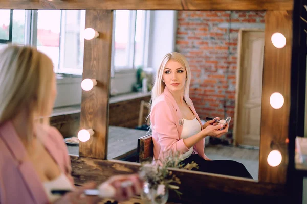 Portrait of a beautiful blonde woman applying makeup near a mirror — Stock Photo, Image