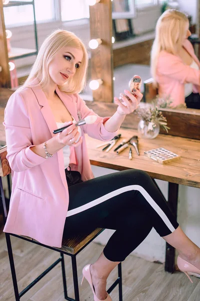 Portrait of a beautiful blonde woman applying makeup near a mirror — Stock Photo, Image