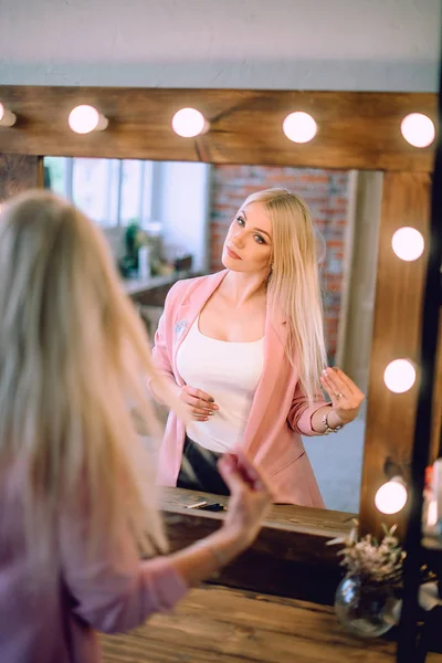 Maquillaje artista positiva hermosa mujer rubia posando cerca del espejo en la sala de maquillaje — Foto de Stock