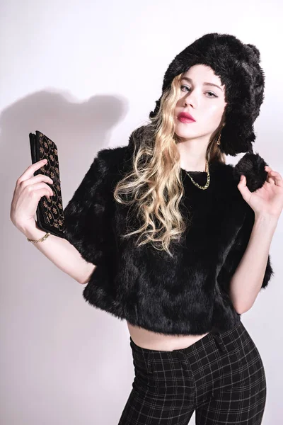 毛皮の帽子と小さな袋を保持している黒のジャケットで美しい若い女性。美しいブロンドの女の子。冬ファッション Beauty.Healthy 髪 — ストック写真