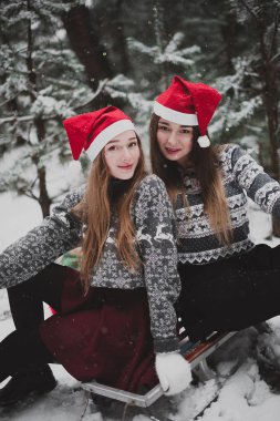 İki genç genç hippi kız arkadaş birlikte. İki kız kardeş hugs moda portre kadar kapatın ve having fun Kış saati, kırmızı santa şapka ve kazak giyen arkadaşlarım açık havada, karlı havalarda Çift