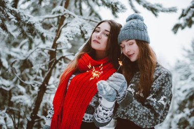 İki genç genç hippi kız arkadaş birlikte. İki kız kardeş hugs moda portre kadar kapatın ve eğleniyor, kazak ve tulum, kış zaman ormanda, maytap tutan arkadaşlarım o çift