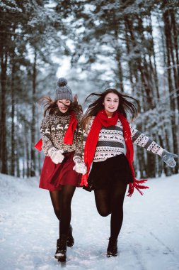 İki genç genç hippi kız arkadaş birlikte. İki kız kardeş hugs moda portre kadar kapatın ve having fun kış zaman ormanda giyen kazak ve tulum, en iyi arkadaş çift açık havada, karlı gitmedenen