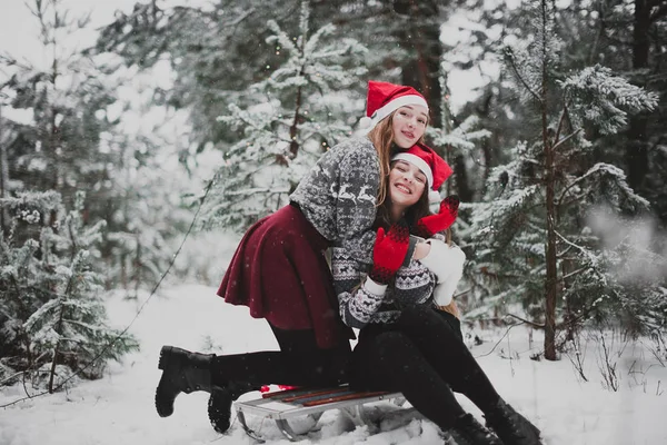 Deux jeunes adolescentes hipster girl friends ensemble.Gros plan portrait de mode de deux sœurs câlins et avoir du plaisir l'hiver, portant chapeaux et pull Père Noël rouge, meilleurs amis couple à l'extérieur, temps neigeux — Photo