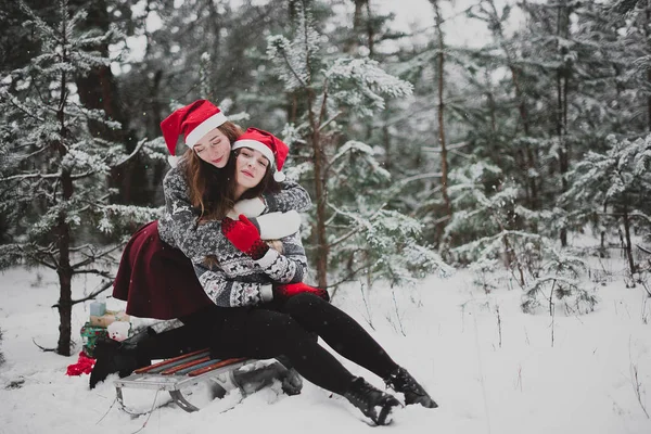 Dois jovens amigos hipster menina adolescente juntos.Close up retrato de moda de duas irmãs abraços e se divertindo tempo de inverno, vestindo chapéus vermelhos do Papai Noel e suéter, melhores amigos casal ao ar livre, tempo nevado — Fotografia de Stock
