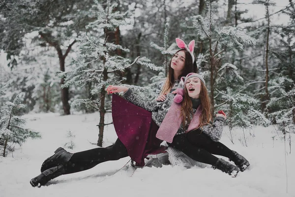 Two young teenage hipster girl friends together.Close up fashion portrait of two sisters hugs and having fun winter time, wearing pink hats, rabbit ears and sweater, best friends couple outdoors, snowy — стоковое фото