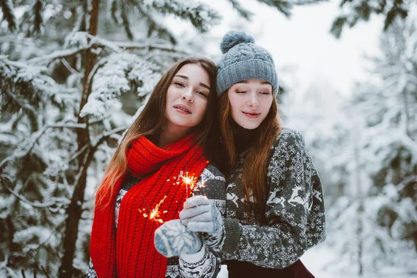 Zwei junge Teenager-Hipster-Freundinnen together.close up Mode Porträt von zwei Schwestern umarmt und Spaß haben, halten Wunderkerzen im Winter Wald, tragen Pullover und Schals, beste Freunde paar o — Stockfoto