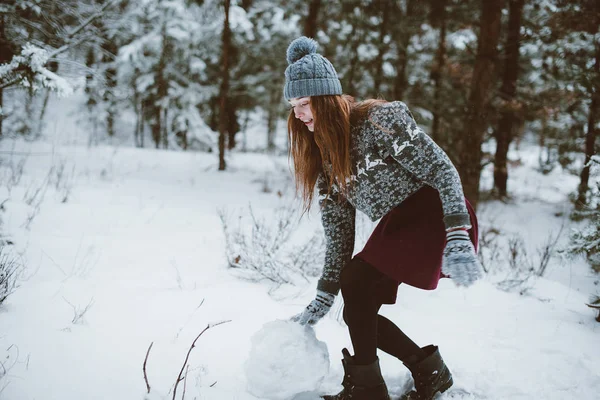 Jovem adolescente hipster menina se divertindo, fazer boneco de neve na floresta tempo de inverno, vestindo suéteres e lenços, ao ar livre, tempo nevado — Fotografia de Stock
