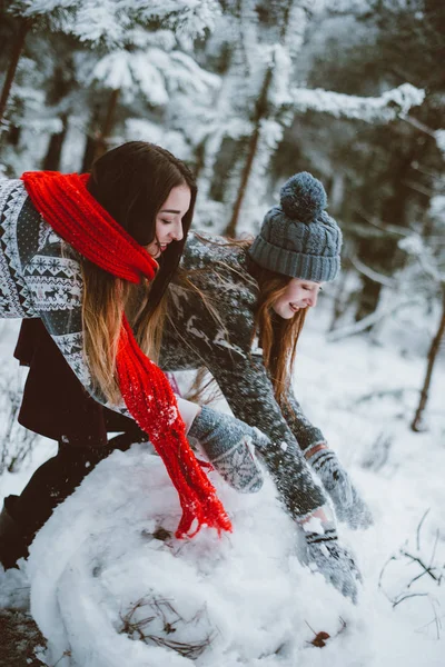 Two young teenage hipster girl friends together.Close up fashion portrait of two sisters hugs and having fun, make snowman in winter time forest, wearing sweaters and scarfs, best friends couple outdoo — стоковое фото