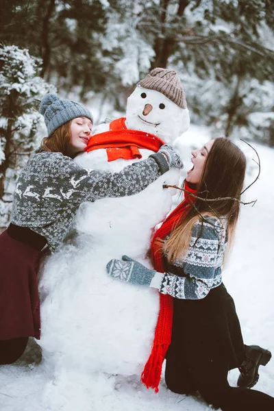 Dwóch przyjaciół dziewczyny młode nastoletnie hipster razem. Moda piękny portret uścisków dwie siostry z bliska i dobra zabawa, zrobić bałwana w lesie czas zimowy, noszenie swetry i szaliki, przyjaciele para outdoo — Zdjęcie stockowe