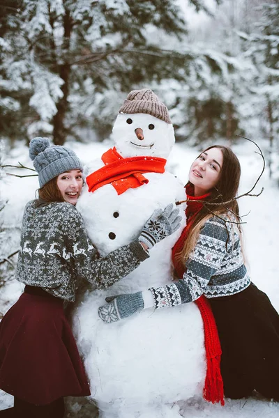 İki genç genç hippi kız arkadaş birlikte. İki kız kardeş hugs moda portre kadar kapatın ve eğlenmek, kardan adam kış zaman orman, kazak ve tulum, en iyi arkadaş çift sıklıkta giyiyor olun