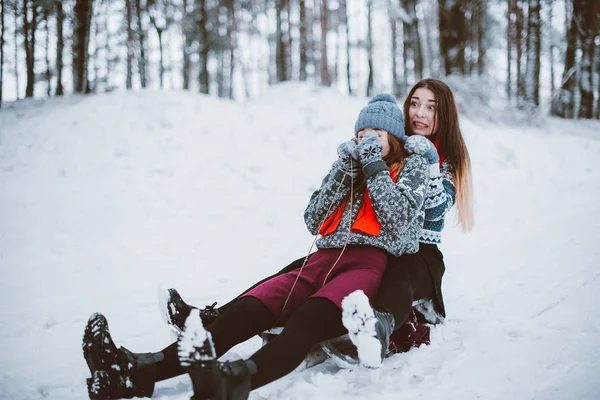 İki genç genç hippi kız arkadaş birlikte. İki kız kardeş hugs moda portre kadar kapatın ve eğlenmek, kazak ve tulum, en iyi arkadaş çift sıklıkta giyen kış zaman ormandaki kızağa binmek
