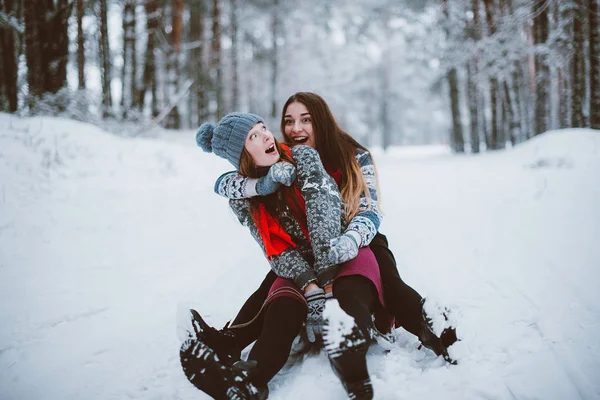 İki genç genç hippi kız arkadaş birlikte. İki kız kardeş hugs moda portre kadar kapatın ve eğlenmek, kazak ve tulum, en iyi arkadaş çift sıklıkta giyen kış zaman ormandaki kızağa binmek