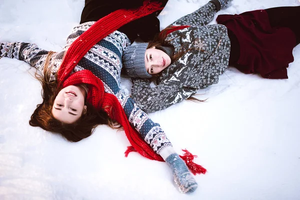 İki genç genç hippi kız arkadaş birlikte. İki kız kardeş hugs moda portre kadar kapatın ve kazak ve tulum, en iyi arkadaş çift açık havada kar kış zaman ormandaki yalan eğleniyor