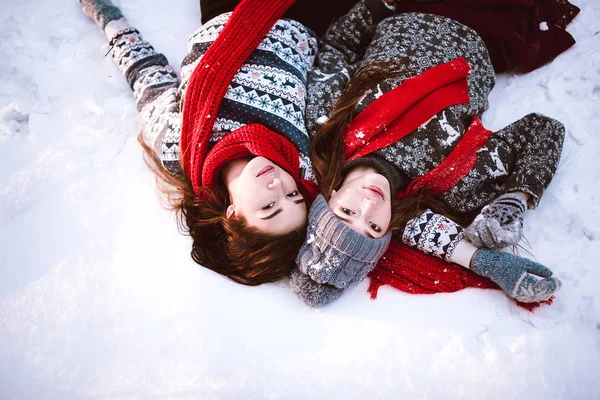 Dois jovens amigos hipster menina adolescente juntos.Close up retrato de moda de duas irmãs abraços e se divertindo mentir na neve na floresta tempo de inverno, vestindo camisolas e lenços, melhores amigos casal ao ar livre — Fotografia de Stock