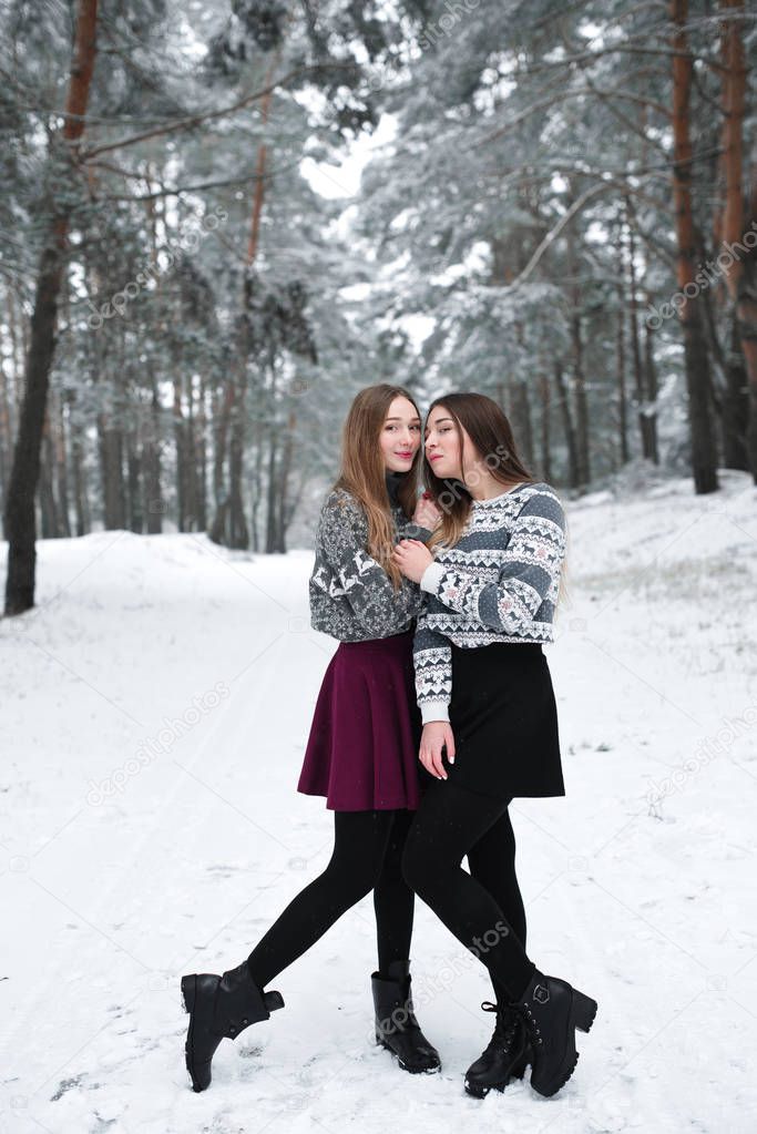 Two young teenage hipster girl friends together.Close up fashion portrait of two sisters hugs and having fun winter time,wearing sweater,best friends couple outdoors, snowy weather