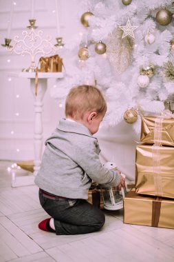 Hediyeler ile oynayan neşeli küçük oğlu ve Noel ağacı, altın ve bej pastel c sunar