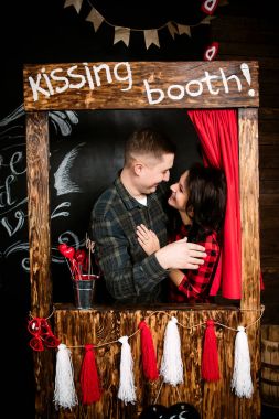 Young cheerful european couple in love embracing in kissing booth, in decorated with hearts studio on valentine day, dating. clipart