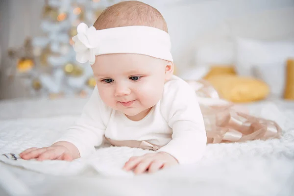 Niña vistiendo lindo vestido y diadema, se encuentra en una cubierta blanca en la habitación festivamente decorada con guirnalda de luces. Con relojes sorpresa en la cámara, sobre un fondo un conjunto de fuegos brillantes. Cálido. — Foto de Stock