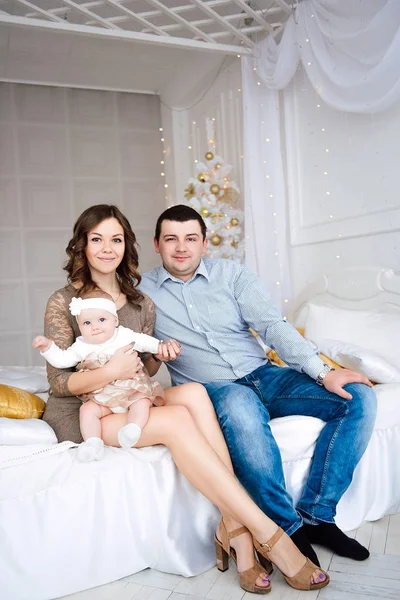 Bebê menina vestindo vestido bonito e headband com mãe e pai, perto da árvore de Natal em quarto festivamente decorado com guirlanda de luzes. Quente bege e ouro cores de Natal e ano novo atmosférico — Fotografia de Stock