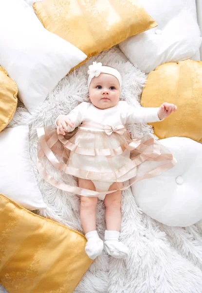 Niña vistiendo lindo vestido y diadema, se encuentra en una cubierta blanca en la habitación festivamente decorada con guirnalda de luces. Con relojes sorpresa en la cámara, sobre un fondo un conjunto de fuegos brillantes. Cálido. — Foto de Stock