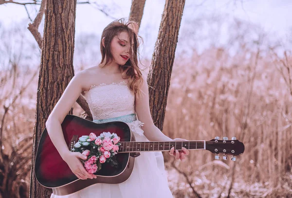 Όμορφη ρομαντική ευρωπαϊκή κοπέλα με κιθάρα με λουλούδια στο εσωτερικό, ποζάροντας σε εξωτερικούς χώρους. Έννοια της μουσικής και της φύσης. Άνοιξη. — Φωτογραφία Αρχείου