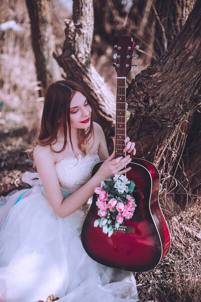 Beautiful romantic european girl with guitar with flowers inside, posing outdoors. Concept of music and nature. Spring time.