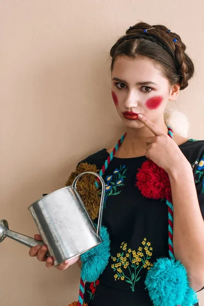 Fashionabla vacker brunett flicka i en jumpsuit med blommiga broderier med färg smink: röda kinder och läppar har roligt, vattna blommor. Mormor chic stil. Retuscherade porträtt — Stockfoto