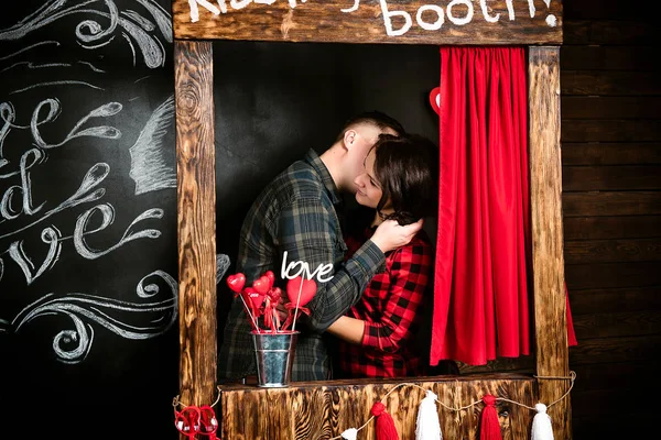 Giovane allegra coppia europea innamorata abbracciando in cabina baci, in decorato con cuori studio il giorno di San Valentino, incontri . — Foto Stock