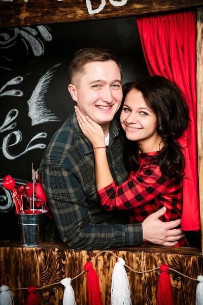 Jovem casal europeu alegre no amor abraçando na cabine de beijos, em decorado com estúdio corações no dia dos namorados, namoro . — Fotografia de Stock