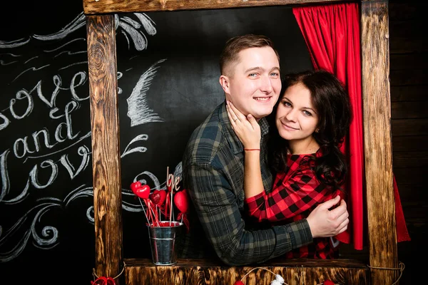 Jovem casal europeu alegre no amor abraçando na cabine de beijos, em decorado com estúdio corações no dia dos namorados, namoro . — Fotografia de Stock