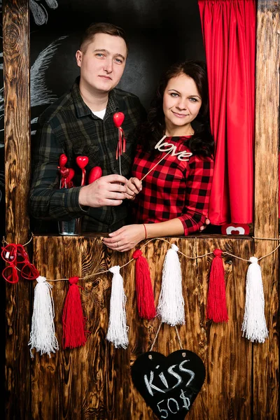 Joven pareja europea alegre en el amor abrazar en cabina de besos, en decorado con corazones estudio en día de San Valentín, citas . —  Fotos de Stock