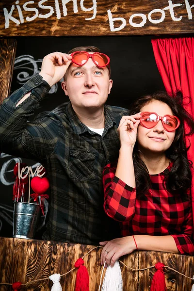 Giovane allegra coppia europea innamorata abbracciando in cabina baci, in decorato con cuori studio il giorno di San Valentino, incontri . — Foto Stock