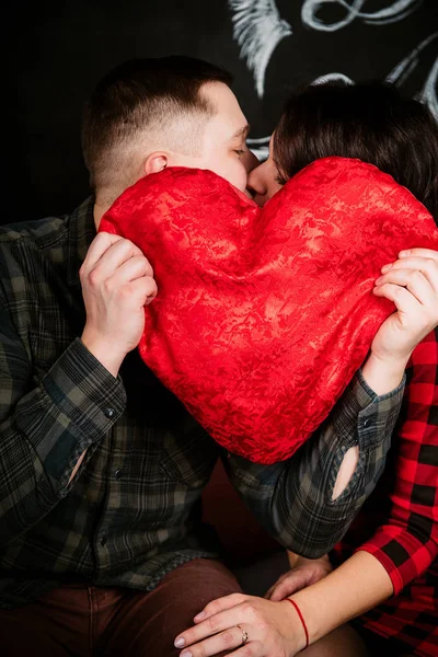 Junges fröhliches europäisches verliebtes Paar, das sich umarmt und küsst, in einem mit Herzen dekorierten Studio am Valentinstag, Datierung. — Stockfoto