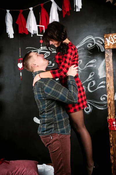 Young cheerful european couple in love embracing and kissing, in decorated with hearts studio on valentine day, dating. — Stock Photo, Image