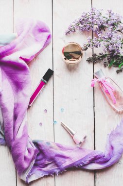 Düz yatıyordu, üst görünüm yaylı masa çerçevesi. Ahşap zemin üzerinde kozmetik, ruj ve leylak çiçekleri olan kadınsı masa çalışma alanı.