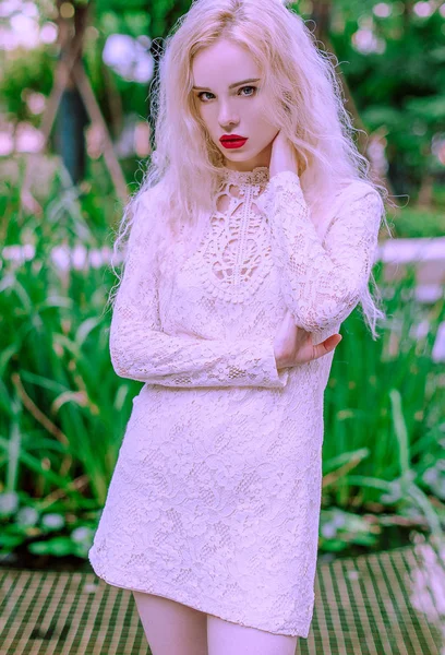 Красива молода блондинка посміхається щаслива жінка з червоними губами в червоному взутті в білій сукні грає біля фонтану в літній день — стокове фото