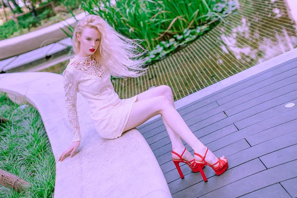 Beautiful young blonde smiling happy woman with red lips in red shoes in a white dress play near a fountain in a summer day Stock Picture