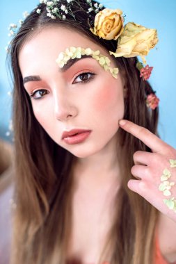 Kozmetik ve manikür. Yakın çekim portre olan kuru çiçekler onun yüz ve saç, pastel renkli, çekici kadın makyaj mükemmel ve mavi arka plan üzerinde deri. Taze, trendy, Bahar düzeltisiz portre