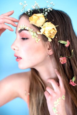 Kozmetik ve manikür. Yakın çekim portre olan kuru çiçekler onun yüz ve saç, pastel renkli, çekici kadın makyaj mükemmel ve mavi arka plan üzerinde deri. Taze, trendy, Bahar düzeltisiz portre
