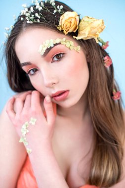 Kozmetik ve manikür. Yakın çekim portre olan kuru çiçekler onun yüz ve saç, pastel renkli, çekici kadın makyaj mükemmel ve mavi arka plan üzerinde deri. Taze, trendy, Bahar düzeltisiz portre