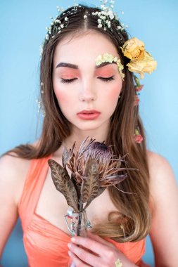 Kozmetik ve manikür. Yakın çekim portre olan kuru çiçekler onun yüz ve saç, pastel renkli, çekici kadın makyaj mükemmel ve mavi arka plan üzerinde deri. Taze, trendy, Bahar düzeltisiz portre