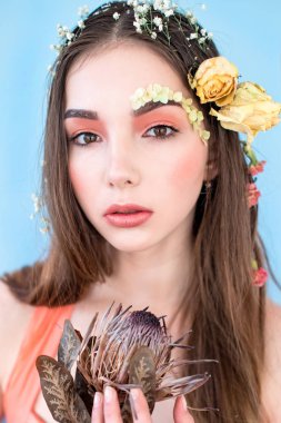 Kozmetik ve manikür. Yakın çekim portre olan kuru çiçekler onun yüz ve saç, pastel renkli, çekici kadın makyaj mükemmel ve mavi arka plan üzerinde deri. Taze, trendy, Bahar düzeltisiz portre